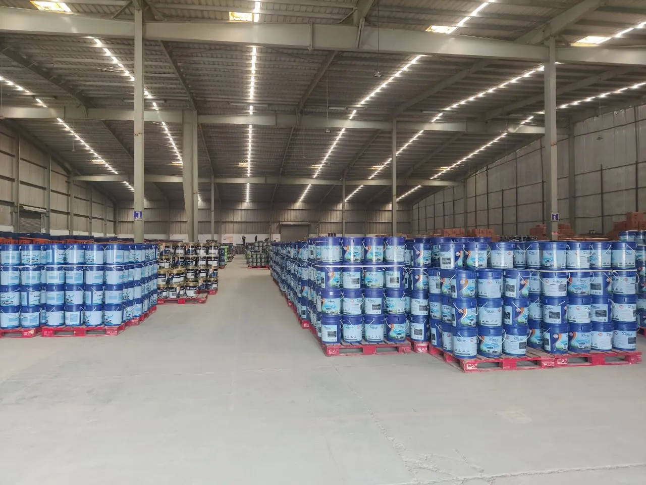 Pallets of lubricant and paint buckets inside a steel-frame warehouse